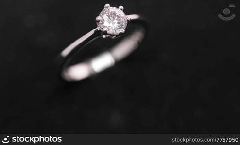 Engagement diamond ring rotating on black background. Traditional piece of jewelry, macro shot. Seamless loop.. Engagement diamond ring rotating, seamless loop