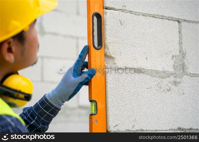 Engi≠er measures the work out wall lightweight concrete blocks with a≤vel at construction site.