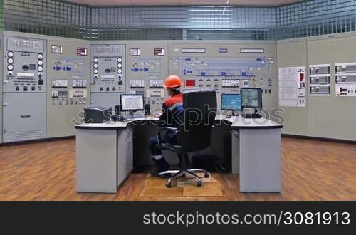 engineer analyzes tables on monitor while sitting in his workplace at main control panel of gas compressor station, wide angle