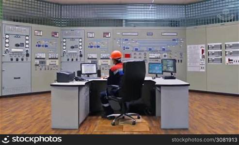 engineer analyzes tables on monitor while sitting in his workplace at main control panel of gas compressor station, wide angle