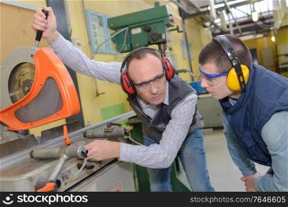 engineer and apprentice using machinery in factory