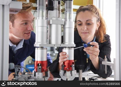 Engineer And Apprentice Working On Machine In Factory