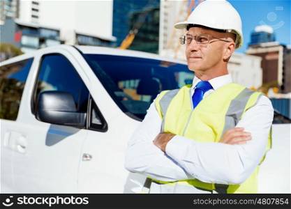 Engineer builder at construction site. Engineer builder wearing safety vest at construction site next to white van
