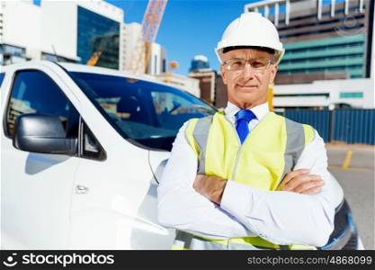 Engineer builder at construction site. Engineer builder wearing safety vest at construction site next to white van