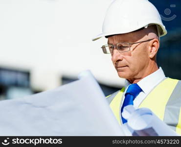 Engineer builder at construction site. Engineer builder wearing safety vest with blueprint at construction site