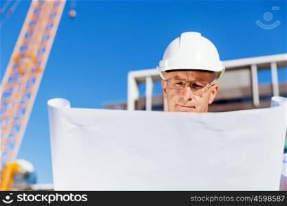 Engineer builder at construction site. Engineer builder wearing safety vest with blueprint at construction site