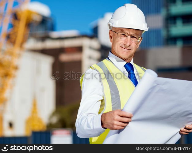 Engineer builder at construction site. Engineer builder wearing safety vest with blueprint at construction site