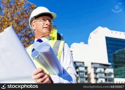 Engineer builder at construction site. Engineer builder wearing safety vest with blueprint at construction site