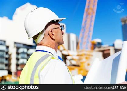 Engineer builder at construction site. Engineer builder wearing safety vest with blueprint at construction site