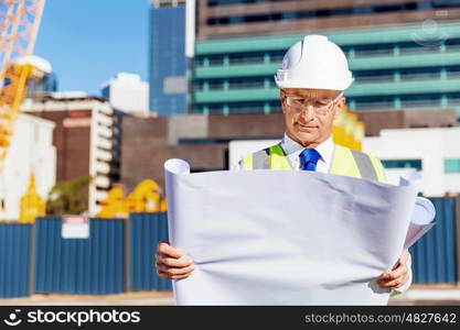 Engineer builder at construction site. Engineer builder wearing safety vest with blueprint at construction site