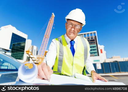 Engineer builder at construction site. Engineer builder wearing safety vest with blueprint at construction site