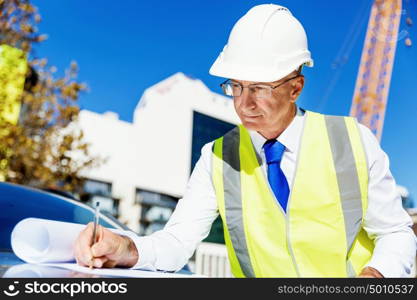 Engineer builder at construction site. Engineer builder wearing safety vest with blueprint at construction site