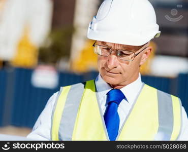 Engineer builder at construction site. Engineer builder wearing safety vest with blueprint at construction site