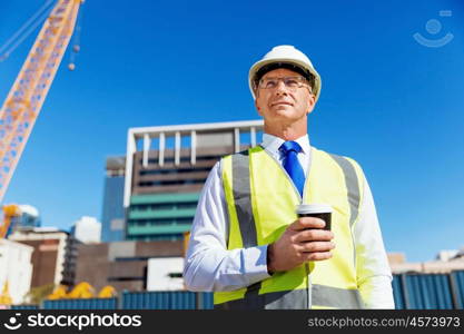 Engineer builder at construction site. Engineer builder wearing safety vest with coffee at construction site