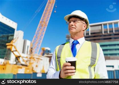 Engineer builder at construction site. Engineer builder wearing safety vest with coffee at construction site