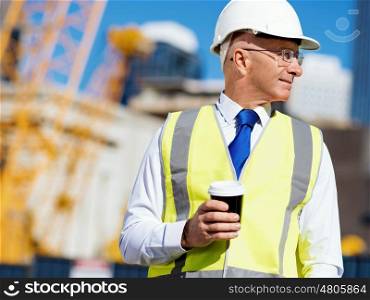 Engineer builder at construction site. Engineer builder wearing safety vest with coffee at construction site