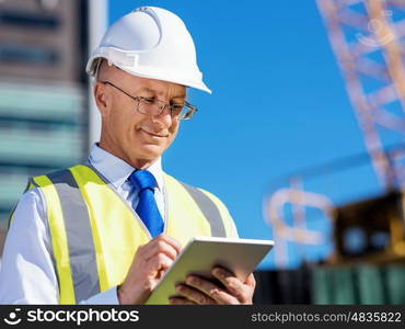 Engineer builder at construction site. Engineer builder wearing safety vest with notepad at construction site