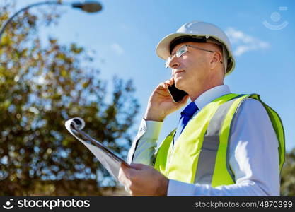 Engineer builder at construction site. Engineer builder wearing safety vest with notepad at construction site