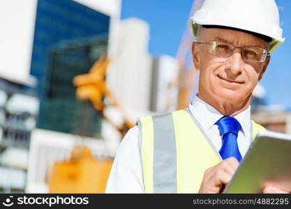 Engineer builder at construction site. Engineer builder wearing safety vest with notepad at construction site