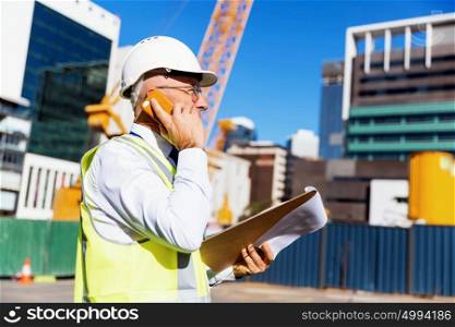 Engineer builder at construction site. Engineer builder wearing safety vest with notepad at construction site
