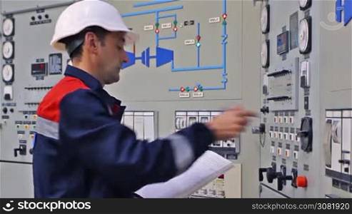 engineer checks thermal sensors and writes into registry near main control panel of gas compressor station, closeup