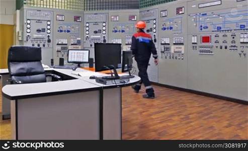 engineer checks thermal sensors on main control panel of gas compressor station and returns to workplace