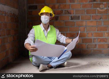 engineer concept The male building maker in full protecting outfits perching on the ground of the building, opening his building diagram, and surveying his eyes on the wall of the building.