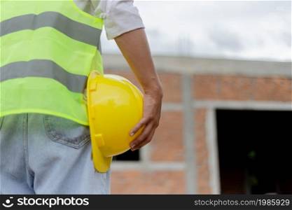 engineer concept The male constructing staff that wears a white top covered with bright lime vest, a black watch, and light blue jeans standing and holding a mustard safety hat.