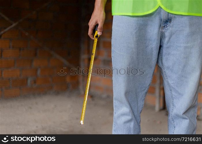 engineer concept The man wearing light shade of jeans standing in the constructing building and handing a tape rule.