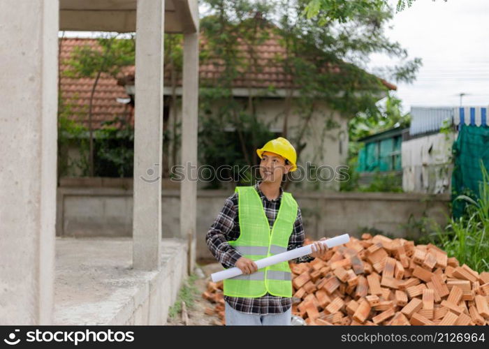 engineer concept The young engineer wearing black plaid shirt covered with light green shirt and a yellow safety helmet pointing at the second floor of the building.