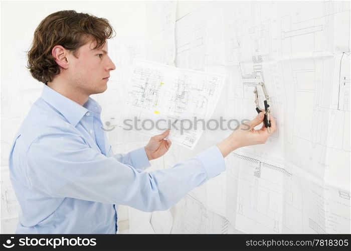 Engineer cross referencing technical drawings with a pair of compasses