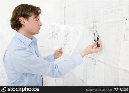 Engineer cross referencing technical drawings with a pair of compasses