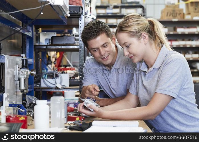 Engineer Helping Female Apprentice In Factory To Measure Component Using Micrometer