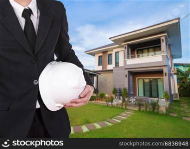 engineer holding helmet with modern house background