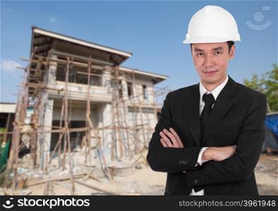 engineer in white helmet with arms crossed, house construction background