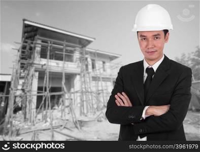 engineer in white helmet with arms crossed, house construction background