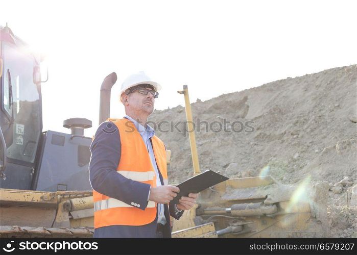 Engineer looking away while holding clipboard at construction site