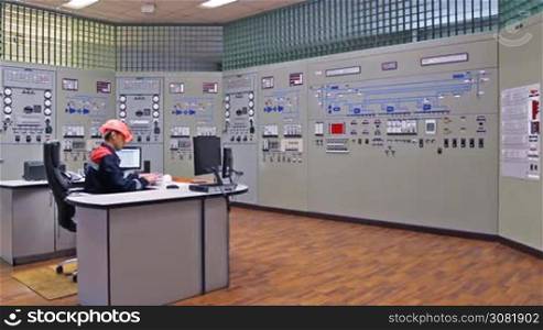engineer looks at monitor and writes down work log near main control panel of gas compressor station, wide angle