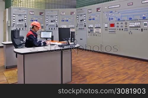 engineer looks at monitor and writes down work log near main control panel of gas compressor station