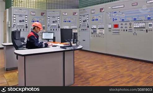 engineer looks at monitor and writes down work log near main control panel of gas compressor station