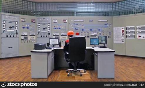 engineer looks at monitor while sitting in his workplace near main control panel of gas compressor station, wide angle