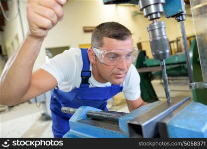 Engineer making hole in metal with bench drill