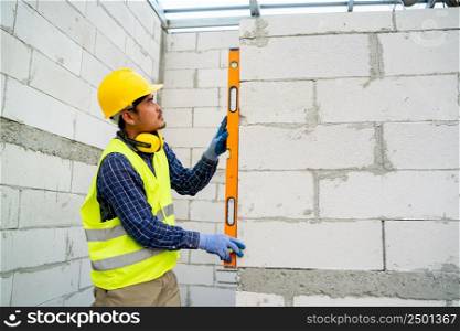 Engineer measures the work out wall lightweight concrete blocks with a level at construction site.