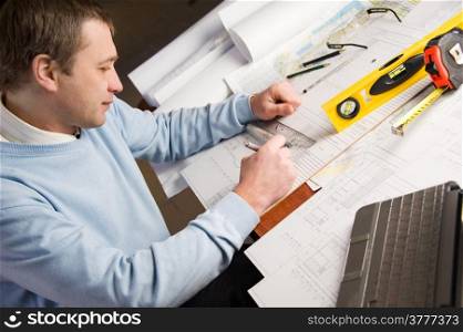 Engineer or architect in blue pullover is working on construction plans.
