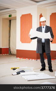 Engineer or architect in the white hard hat with the blueprint. Reconstruction interior.