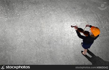 Engineer play violin. Top view of businesswoman in helmet playing violin