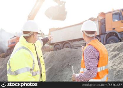 Engineer pointing at vehicles while discussing at construction site