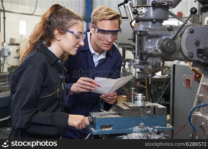 Engineer Showing Apprentice How to Use Drill In Factory