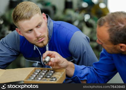 engineer showing metal components to apprentice