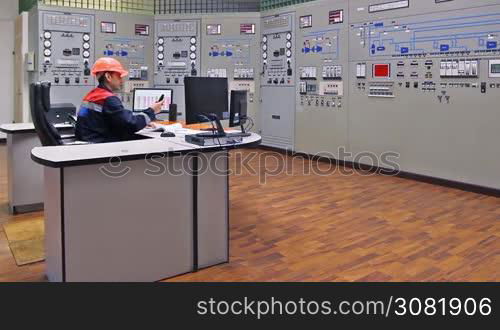 engineer sits and talks on phone at main control panel of gas compressor station